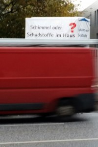 Foto eines vorüberfahrenden roten Lasters vor einer Werbung zur Schimmelbekämpfung