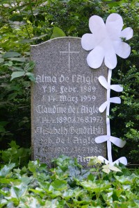 Alma de l'Aigles Grabstein in Niendorf mit Papierblume, die sämtliche falschen S- Buchstaben am Ende des Namens verdeckt