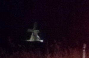 Nachtaufnahme: Foto einer geisterhaft beleuchteten Mühle am Straßenrand.