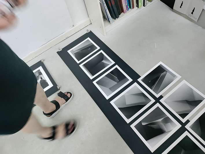 Zwei Fotoreihen von Sabine Höpfner, eine davon von Füßen verdeckt, auf dem grauen Boden eines Ateliers.